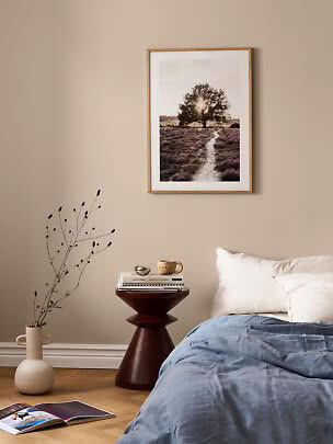 Soveværelse med indrammet naturplakat over sengen, sidebord, vase og blå dyne