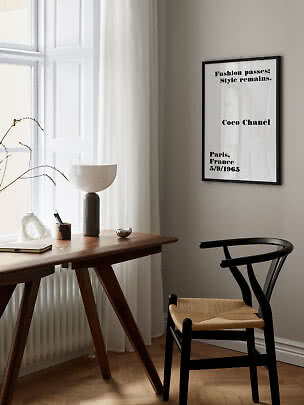 Indrammet Coco Chanel-typografiplakat på væg over træbord ved vindue og sort stol