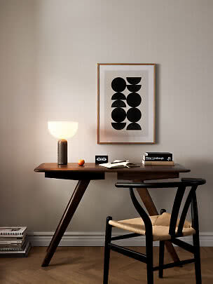 Bureau en bois foncé avec chaise noire, lampe allumée et affiche abstraite au mur