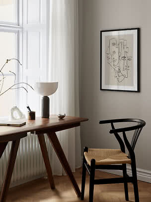 Minimalistisk hjemmekontor med træskrivebord, sort stol, bordlampe og abstrakt vægkunst ved vindue