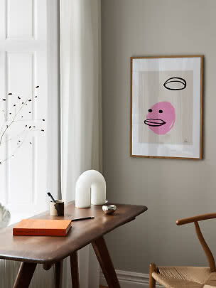 Gerahmtes abstraktes Poster mit rosa Gesicht über einem Holzschreibtisch in hellem Raum