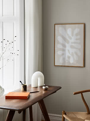 Minimalist corner with wooden desk, abstract wall art, white lamp, book and chair by window