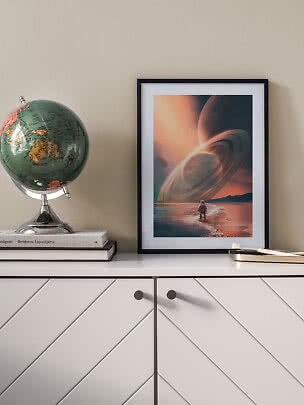 Poster sci-fi incorniciato con pianeta ad anelli sulla spiaggia, su mobile bianco accanto a un globo