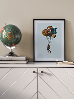 Framed print of an astronaut lifted by planet balloons on a white cabinet beside a globe