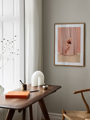 Stampa d’arte incorniciata con donna su cubo rosa davanti a tende rosa su parete beige