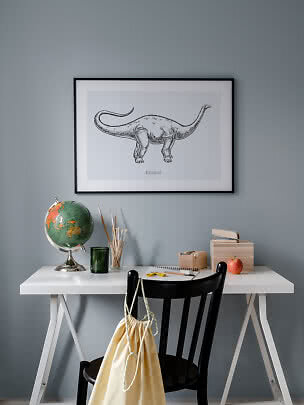 Affiche encadrée de Diplodocus au-dessus d’un bureau blanc avec globe, pinceaux, livres et pomme