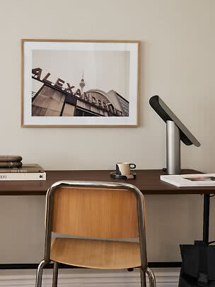Dunkler Holzschreibtisch mit Stuhl, Lampe, Büchern, Tasse und gerahmtem Fotodruck an der Wand