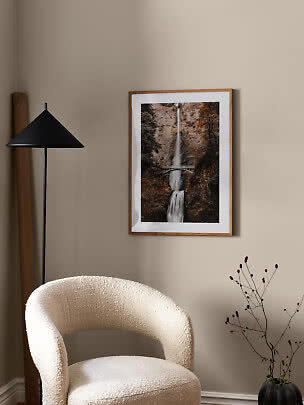 Framed waterfall poster with bridge on a beige wall in a cozy interior corner