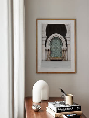 Framed photo of an ornate arch on a beige wall above a wooden table with books and decor