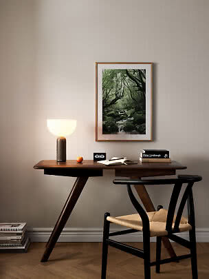 Mørk træskrivbord med stol, bordlampe og indrammet skovfoto på væggen