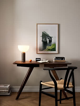 Dark wooden desk with chair, table lamp, books, and framed seascape print on the wall