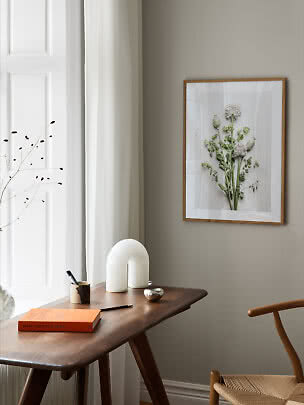 Træindrammet blomsterplakat på beige væg over skrivebord i lyst, minimalistisk rum