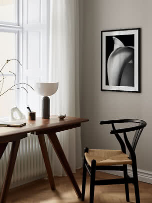 Angolo lavoro minimalista con scrivania in legno, sedia nera, lampada da tavolo e stampa in bianco e nero