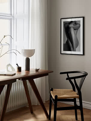 Black-framed black-and-white art print above a wooden desk by a window