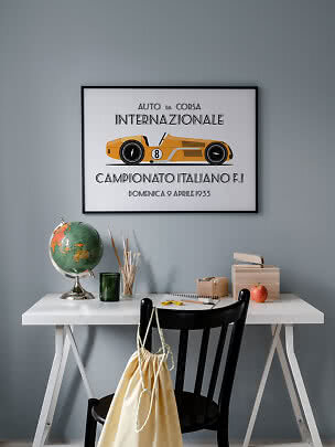 Framed poster of a yellow vintage race car above a white desk against a gray wall