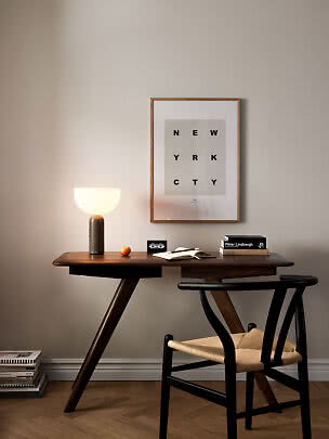 Skrivbord i mörkt trä med tänd bordslampa, stol, böcker och inramad poster på väggen