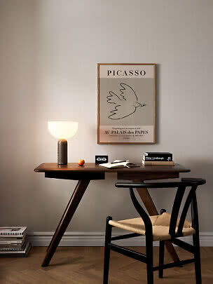 Scrivania in legno scuro con sedia nera, lampada accesa e poster di Picasso incorniciato