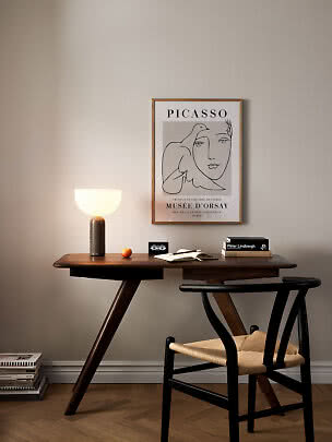 Dark wooden desk with lamp, chair, books and framed Picasso poster on beige wall