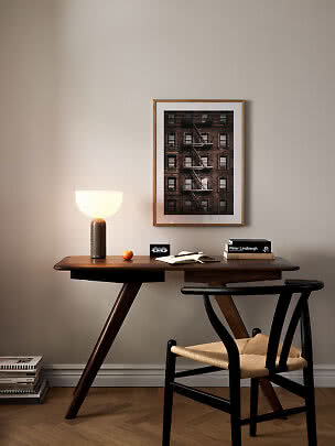 Scrivania in legno scuro con lampada accesa, sedia, libri e foto incorniciata alla parete
