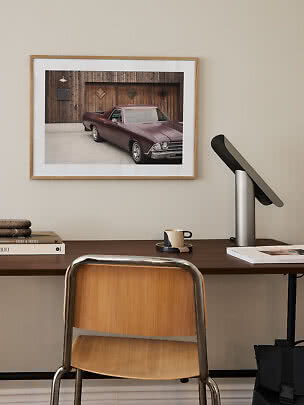 Home office with wooden chair, desk lamp, and framed photo of a classic car on the wall