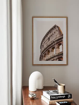 Stampa incorniciata del Colosseo sopra un tavolo in legno con libri, tazza e scultura bianca
