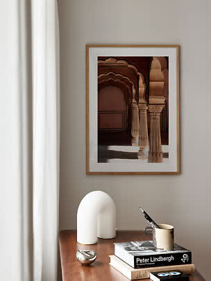 Stampa architettonica incorniciata con archi e colonne sopra un tavolo in legno con libri e decori.