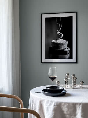 Framed black-and-white print of a corkscrew in a cork above a dining table