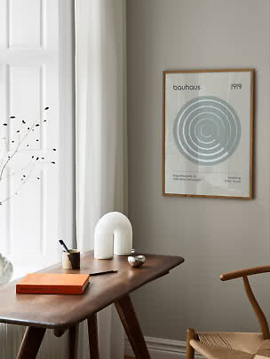 Minimalistischer Arbeitsplatz mit Holztisch, weißer Lampe und Bauhaus-Poster an grauer Wand