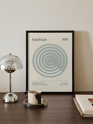 Gerahmtes Bauhaus-Poster mit grauen Kreisen auf einem Tisch neben Chromlampe, Tasse und Buch