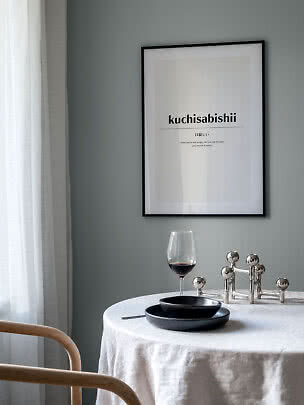 Inramad typografisk poster ovanför ett runt bord med vinglas, svarta tallrikar och ljusstake.