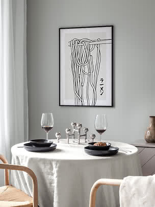 Spisebord med hvid dug, sorte tallerkener, vinglas og indrammet abstrakt plakat på grå væg