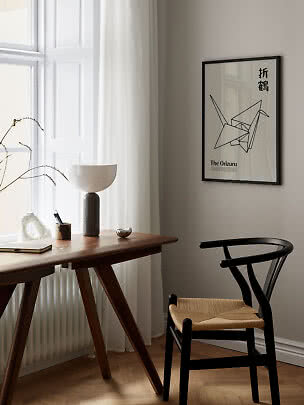 Minimalistisk hjemmekontor med træbord, sort stol, bordlampe og indrammet origami-plakat.