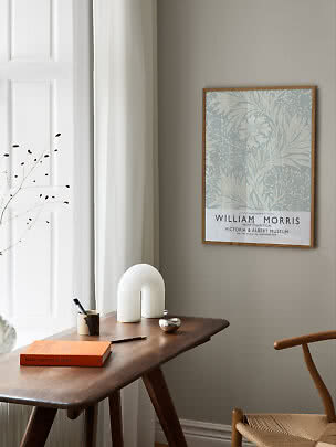 Póster floral de William Morris enmarcado sobre una mesa de madera en una estancia luminosa