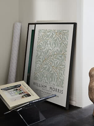 Indrammet William Morris-plakat med bladmotiv lænet op ad væggen ved siden af bøger