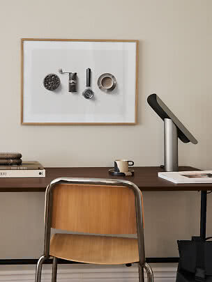 Hjemmekontor med træstol, mørkt skrivebord, moderne lampe og indrammet kaffeplakat på væggen