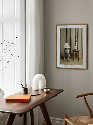 Gerahmter Kunstdruck an beiger Wand über Holztisch in hellem, minimalistischem Raum