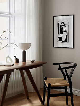 Minimalistisk hjemmekontor med træbord, sort stol, vase og abstrakt sort-hvid plakat.