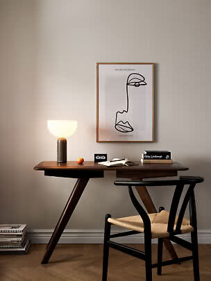 Wooden desk with black chair, lit table lamp, open notebook and framed wall art