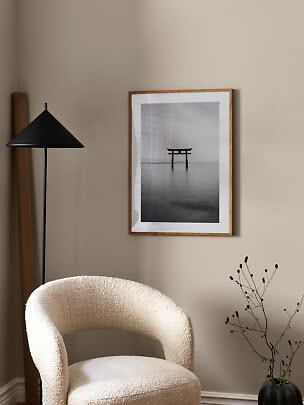 Minimalist room corner with a cream armchair, black floor lamp, and framed black-and-white print.