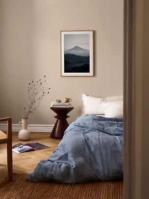 Gemütliches Schlafzimmer mit blauer Bettdecke, weißen Kissen, kleinem Beistelltisch und gerahmtem Bergbild