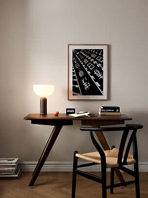 Træskrivebord med sort stol, bordlampe og indrammet sort-hvid plakat på beige væg