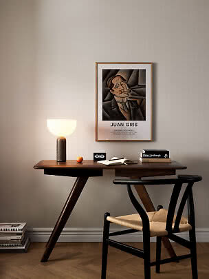 Holzschreibtisch mit schwarzem Stuhl, leuchtender Tischlampe und gerahmtem Juan-Gris-Poster an der Wand