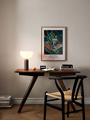 Scrivania in legno scuro con lampada accesa, sedia, libri e quadro incorniciato a parete