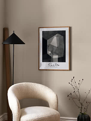 Affiche abstraite noir et blanc encadrée de bois sur mur beige au-dessus d'un fauteuil bouclé clair.