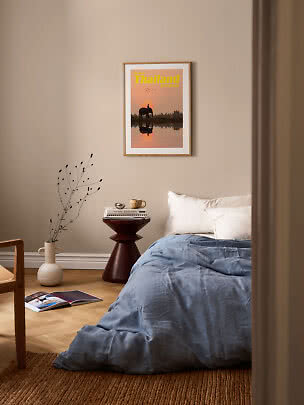 Affiche encadrée de la Thaïlande au-dessus d’un lit, avec linge bleu et petite table