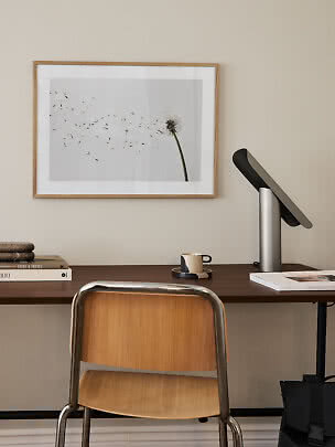 Bureau minimaliste avec chaise en bois, lampe et affiche de pissenlit encadrée au mur