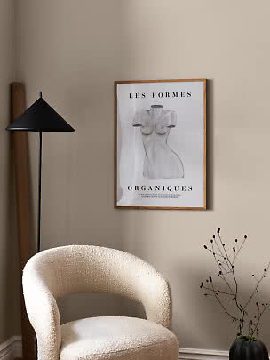 Minimalist room corner with bouclé chair, black floor lamp and framed art poster on beige wall