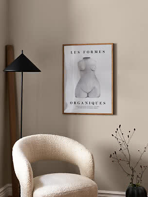 Cozy corner with cream armchair, black floor lamp and framed art print on a beige wall