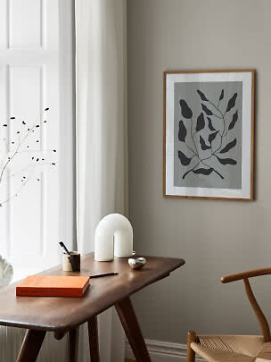 Indrammet botanisk kunstprint over træbord med bog, penneholder og hvid dekorativ lampe.