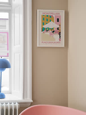 Gerahmtes Montpellier-Poster an beiger Wand neben Fenster mit pastellfarbener Caféplatz-Illustration